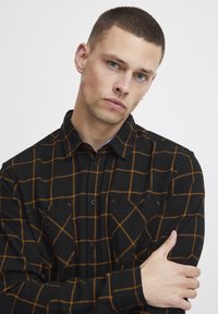Czarna i pomarańczowa flanelowa koszula w kratę z zapięciem na guziki, dwoma kieszeniami na piersi i długimi rękawami. Miękka tekstura i luźny krój.