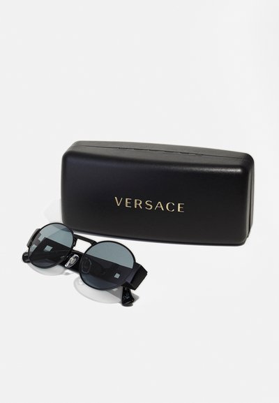 Versace päikeseprillid ümmarguste mustade läätsede, musta raami ja reguleeritava rihmaga. Tuleb koos musta karbiga, millel on kuldne kiri.