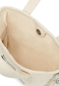 Geantă din pânză în bej deschis, cu interior neted, închidere prin capse și mânere scurte. Prezintă cusături discrete și un design tematic.