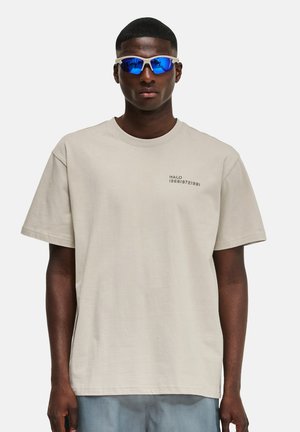 Lys beige bomulds t-shirt med korte ærmer og en rund halsudskæring, med "HALO 196819721981" trykt i sort på brystet.