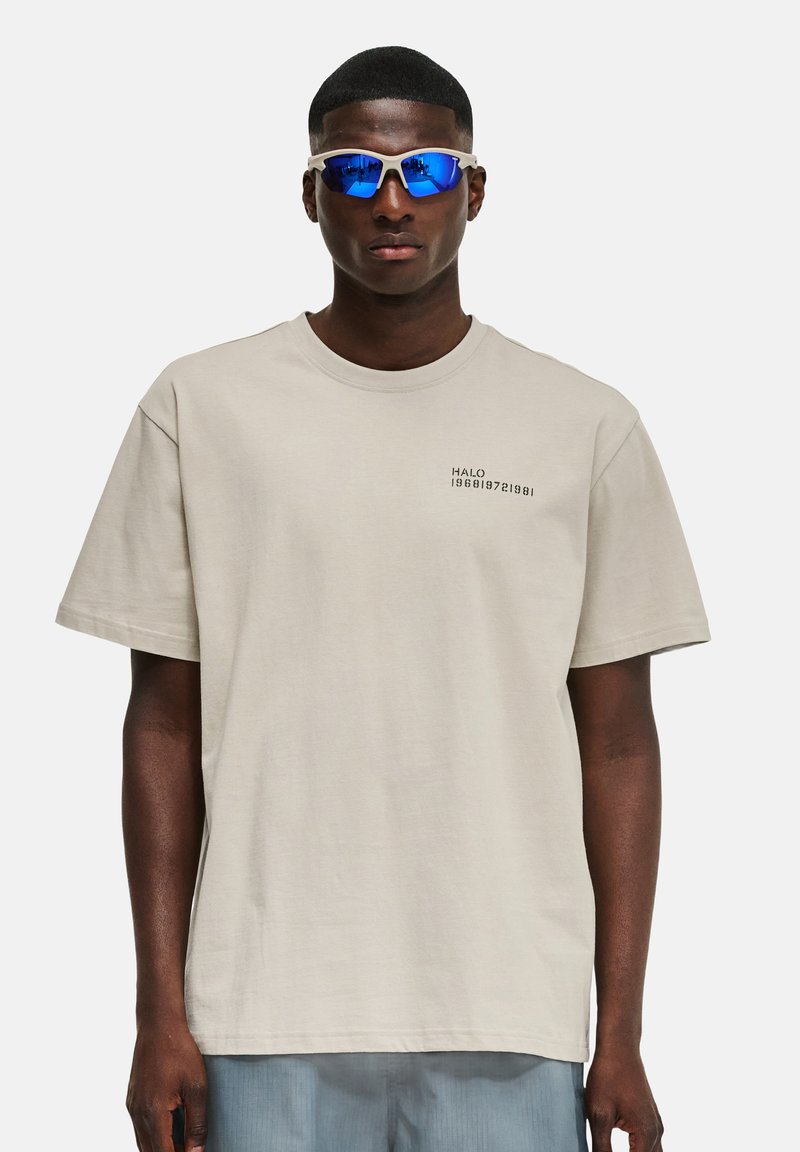 Jasno beżowa bawełniana koszulka z krótkim rękawem i okrągłym dekoltem, z czarnym nadrukiem "HALO 196819721981" na piersi.