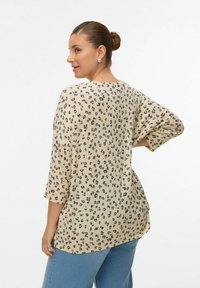 Haut beige avec imprimé animalier noir, coupe ample, manches trois-quarts, ourlet arrondi ; porté avec un jean bleu clair. Tissu doux et texturé.