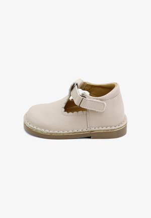 Zapato infantil de cuero beige con recorte en forma de ondas, correa ajustable de gancho y bucle, y suela de goma cosida, mostrado desde el lado izquierdo sobre fondo blanco.