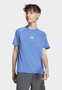 Modrá sportovní tričko s krátkým rukávem, vyrobené z tkaniny odvádějící vlhkost. Obsahuje malé bílé logo na hrudi a má uvolněný střih.