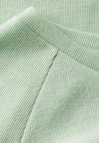 Ljust grönt texturerat tyg med ett ribbat mönster och slät yta. Närbild som fokuserar på sömmarnas detaljer och det mjuka materialet.