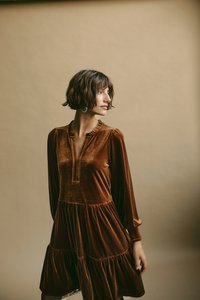 Braunes Samtkleid mit langen Ärmeln, Rüschenausschnitt und gestuftem Rock. Weiche Textur und reiche Farbe mit subtiler Glanz. 