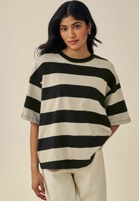 T-shirt surdimensionné noir et crème à rayures avec des manches courtes, un col rond et une coupe décontractée. Associé à un pantalon clair.