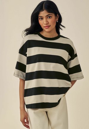 Zwarte en crèmekleurige gestreepte oversized t-shirt met korte mouwen, ronde halslijn en een relaxte pasvorm. Gecombineerd met lichtgekleurde broeken.