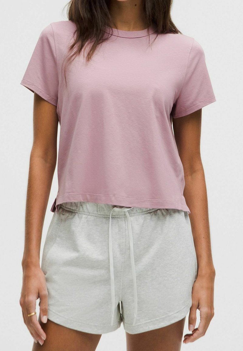Světle růžové bavlněné tričko s krátkým rukávem a volným střihem, doplněné světle šedými šortkami se šňůrkou. Texturovaná měkká tkanina.