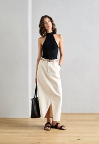 Black sleeveless top, cream-colored denim midi skirt with a side slit, floral belt, black flat sandals, and a black tote bag.