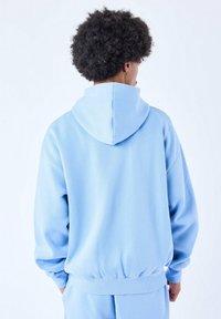 Sudadera con capucha azul claro de ajuste relajado, puños y dobladillo acanalados. Textura suave, sin patrones ni herrajes visibles.