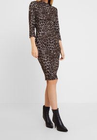 Kleid mit Leopardenmuster, drei Viertelärmeln, figurbetonter Silhouette und knielanger Länge. Kombiniert mit schwarzen, spitzen Ankle-Boots.