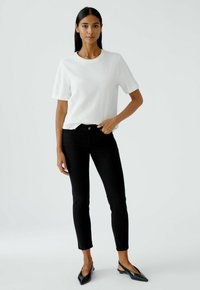 Weißes Kurzarm-T-Shirt aus Baumwolle kombiniert mit schwarzen, eng anliegenden Jeans und schwarzen spitzen Ballerinas. Einfaches Design mit klassischer Silhouette.