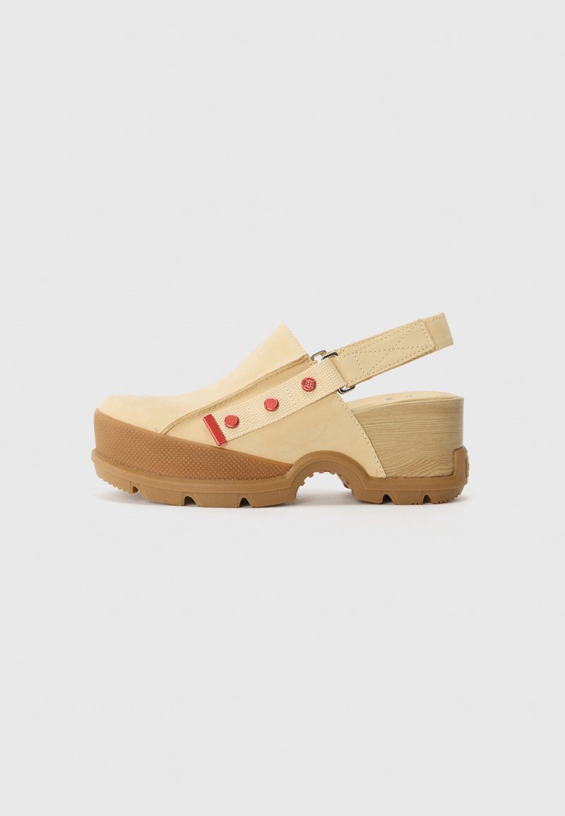 Beige suède klomp met houten blokhak, robuuste bruine zool, verstelbare slingbackriem en rode knoopdetails op de riem.