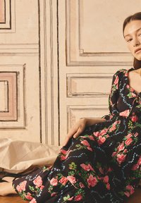 Rochie neagră cu flori, având trandafiri roz și frunze verzi, cu un corset elastic și fustă fluidă. Material fin cu accente decorative.