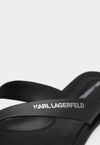 Μαύρο σανδάλι τύπου σαγιονάρας με το λογότυπο "KARL LAGERFELD" σε λευκό χρώμα στον ιμάντα, πάνω σε απλό λευκό φόντο.
