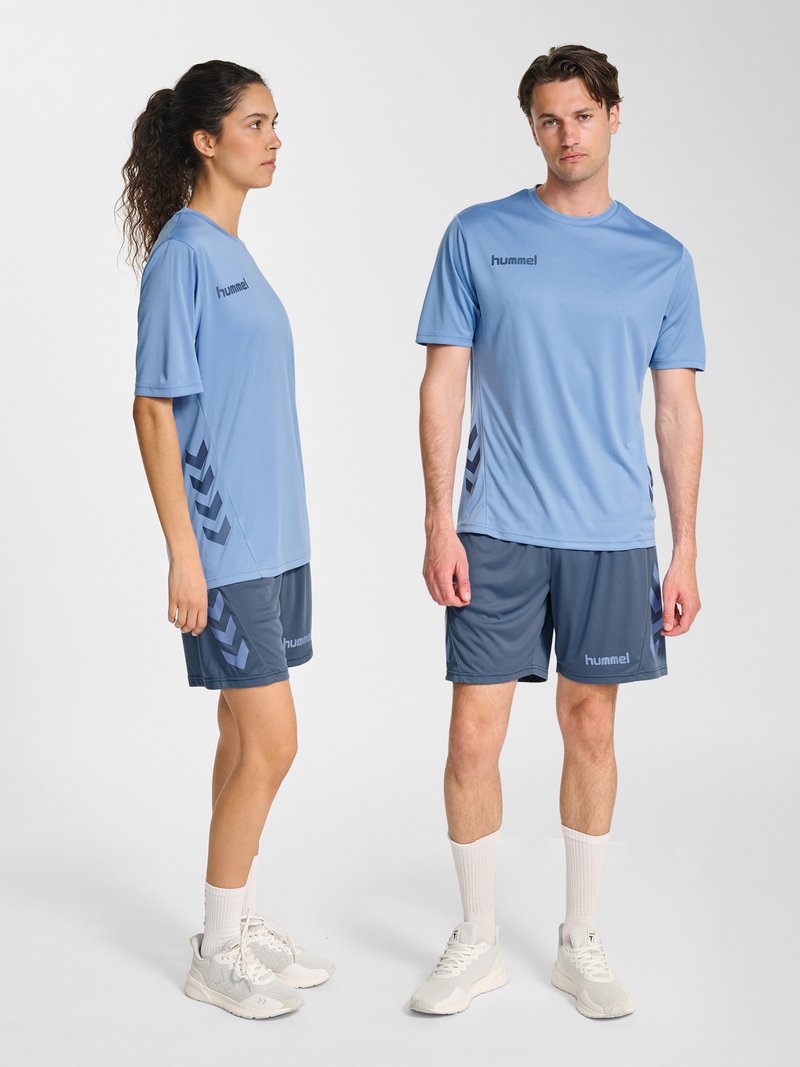Een man en een vrouw die bijpassende lichtblauwe sportshirts en donkerblauwe shorts met hummel-logo's dragen, staand op een witte achtergrond.