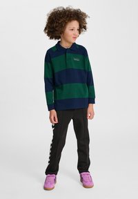 Blå och grönrandig långärmad polo skjorta med krage, kombinerad med svarta byxor med vita sidopaneler och rosa sneakers.