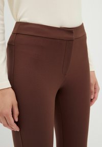 Bruine stretchstof broek met een gladde textuur, voorzien van een slim fit, platte tailleband en zijzakdetails.