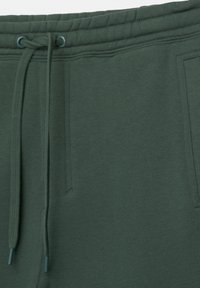 Nahaufnahme des Taillenbundes von dunkelgrünen Sweatpants mit Kordelzug und Seitentaschen, die Nähdetails und Gewebestruktur zeigen.
