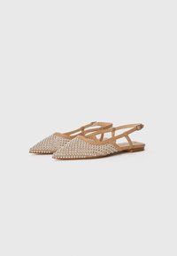 Tan slingback flats with pointed toes, adorned with silver studs arranged in a diamond pattern on the upper. Flat sole, adjustable straps.