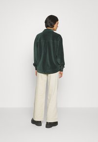 Groene corduroy blouse met knoopmouwen, gedragen met crèmekleurige brede broek en zwarte platformlaarzen. Soepele textuur met verticale ribbing.