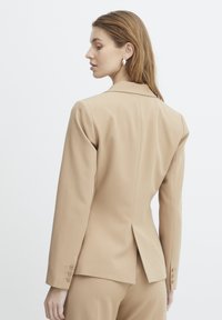 Beige op maat gemaakte blazer met een reverskraag, enkele split aan de achterkant en manchet met drie knopen. Gladde stof met een rechte silhouet.
