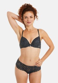 Soutien-gorge en dentelle noire et culotte assortie, présentant des motifs floraux, des finitions délicates, des bretelles réglables et un détail décoratif central.