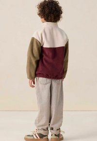 Veste en polaire avec un col montant, dotée de blocs de couleurs beige, vert olive et bordeaux. Associée à un pantalon ample gris clair et des baskets.
