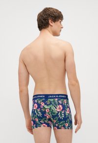 Férfi boxer alsónadrág sötétkék virágmintával, rózsaszín hibiszkuszokkal és zöld levelekkel. Jellemzője a kék elasztikus derékpánt, amelyen a márkaneve olvasható.