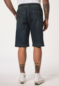 Pantalones cortos de mezclilla en azul oscuro con una cintura elástica, dos bolsillos traseros con botones y un corte recto que termina justo encima de la rodilla.