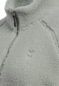 Lichtgrijze fleece jack met ritssluiting en hoge kraag, met een gestructureerd oppervlak en een geborduurde logo aan de voorkant.