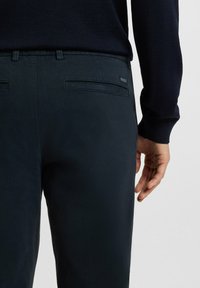 Navy blue trousers made of a smooth fabric, featuring belt loops, back pockets, and a subtle logo label on the waistline.