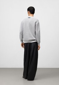 Grijze gebreide trui met een gestructureerde afwerking, ronde halslijn en zwart label aan de achterkant, gecombineerd met hoge taille zwarte wijde broek.
