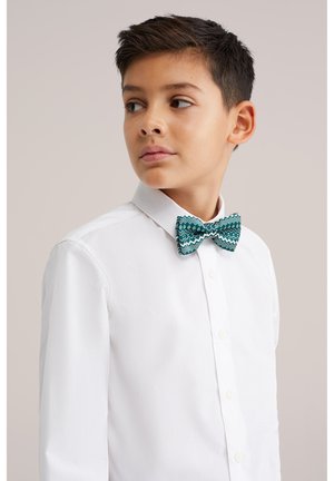 Peteliškė turkio spalvos su zigzago ir rombų raštais, derinama su balta mygtukais užsegama palaidine. Lygus audinys su klasikine forma.