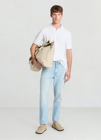Sac en toile beige avec fermeture à ruban, porté par une personne portant un polo blanc, un jean bleu clair et des chaussures beige à enfiler.