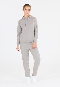 Grauer Hoodie mit verstellbaren Kordeln und Kängurutasche, kombiniert mit passenden grauen Jogginghosen, beide aus weichem Stoff. Weiße Sneaker.