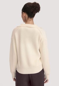 Cremefarbener Pullover mit gerippter Textur, oversize Passform und weiter Kragen. Verfügt über lange Ärmel und einen schmalen Saum.