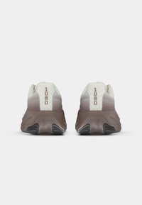 Une paire de chaussures de course gris clair et marron vue de l'arrière, avec des semelles surélevées et "1080" imprimé à l'arrière.