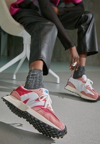 Baskets athlétiques roses et blanches avec une semelle noire épaisse, en suède et mesh, lacets détaillés, et accents bleus sur la languette.