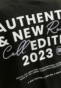 Μαύρο ύφασμα με λευκό και γκρι κείμενο που γράφει "Authentic & New Edition 2023" και μικρότερο κείμενο για την ψηφιακή καλλιτεχνική διεύθυνση από το JREBEL Collective.