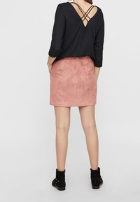 Top nero con schiena a V profonda e spalline incrociate; abbinato a una mini gonna in suede rosa pallido con dettaglio zipper e stivali neri alla caviglia.