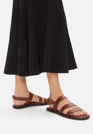 Sandali in pelle marrone con tre cinture orizzontali e una fibbia regolabile. Presentano una suola piatta e un design con punta aperta.