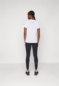 Biela košeľa s krátkym rukávom a logom, skombinovaná s čiernymi legginsami. Zaujímavé detaily zahŕňajú priliehavý strih a textúrovanú látku. Jemné branding na nohaviciach.