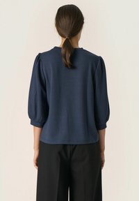 Navyblauwe pullover top met puffmouwen en een ronde halslijn, gemaakt van zachte stof, gecombineerd met zwarte wijde broek.