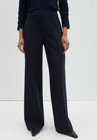 Pantalon à jambes larges en bleu marine foncé, présentant une coupe ajustée, une taille haute et un tissu lisse. Comprend des plis à l'avant et des poches latérales discrètes.