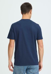 Laivastonsininen puuvillainen T-paita, jossa on lyhyet hihat ja pyöreä pääntie. Takakuvassa näkyy sileä pinta ja rento istuvuus.