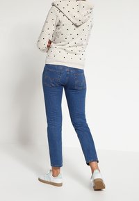 Sudadera con capucha gris claro con patrones de corazones negros, jeans de mezclilla azul y zapatillas blancas con detalles en verde menta en el talón.