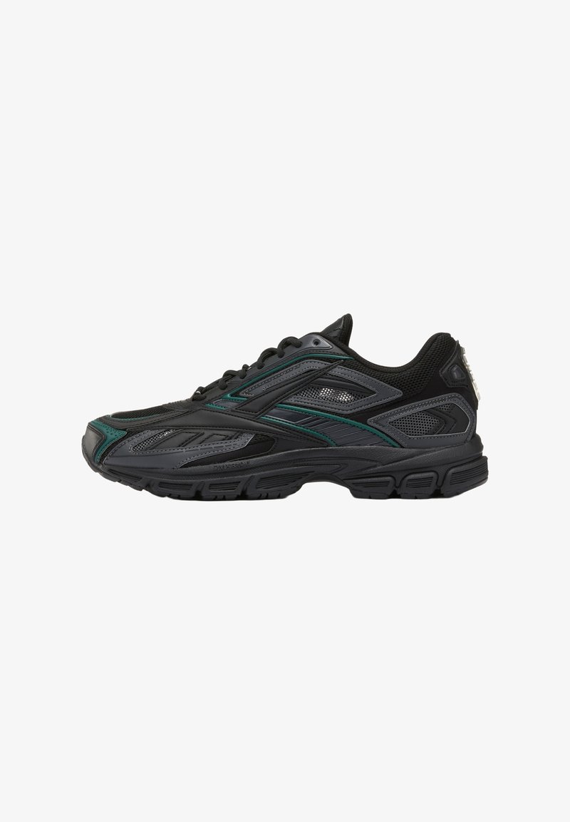 Baskets de sport noires avec accents verts, panneaux en mesh et semelle texturée, vues de profil sur un fond blanc.