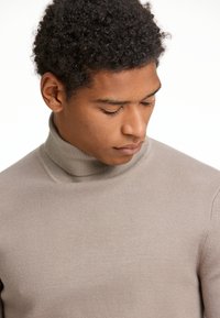 Beiger Rollkragenpullover mit gerippter Textur und taillierter Passform, der einen hohen Kragen und subtile Nähte aufweist.